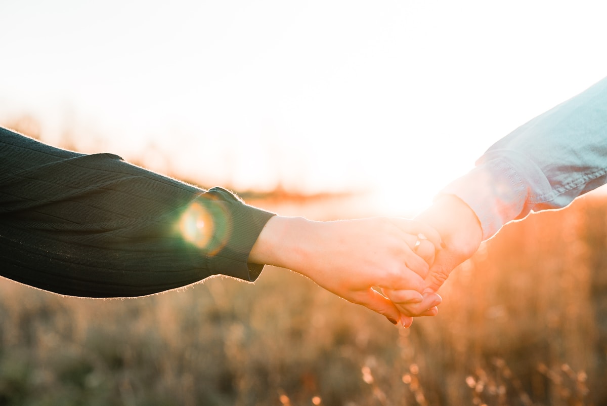 Duas pessoas de mãos dadas sob a luz do fim de tarde